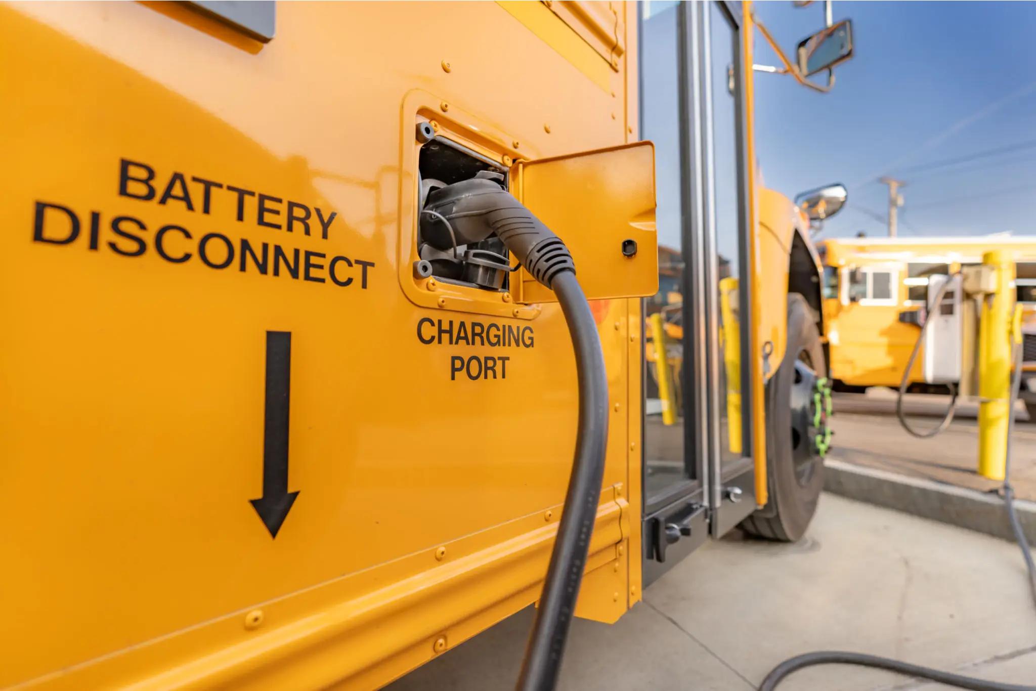 Close-up of an electric school bus being charged at a charging station, with charging cable connected to the charging port.