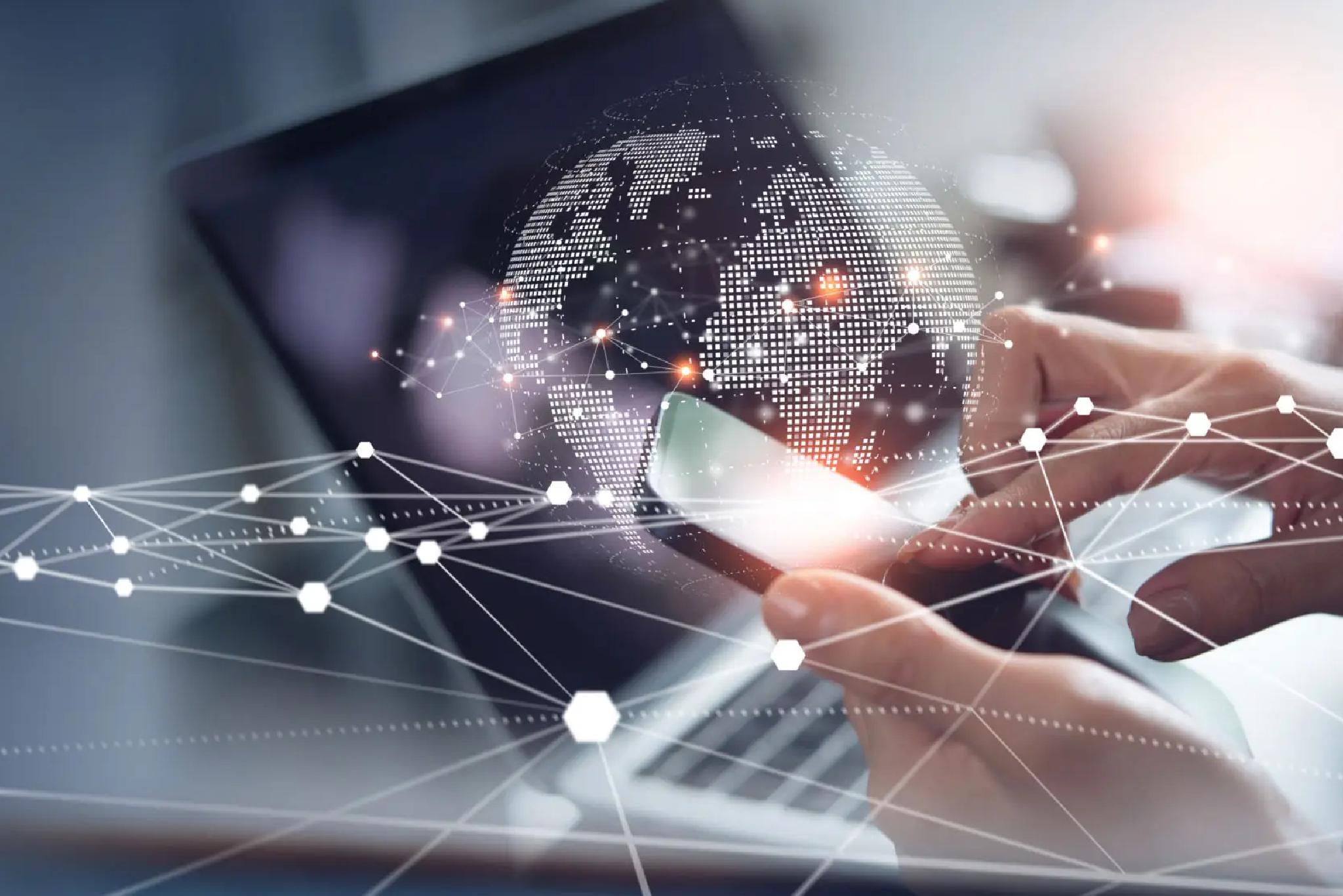 A person uses a smartphone with a laptop in the background, overlaid with digital graphics of a world map and network connections.