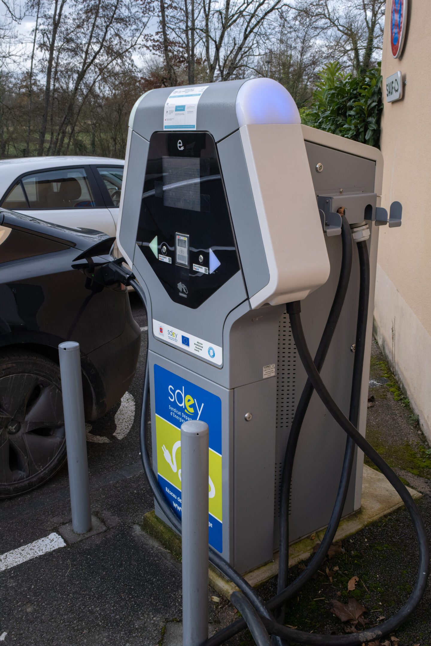 Moulins-sur-Ouanne, France - February 24, 2022: A static shot of a solid black Tesla Model 3 dual motor charging at the DC Freshmile charging station in a cloudy winter day. Selective focus